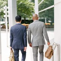 Two men in suits walking down a sidewalk.